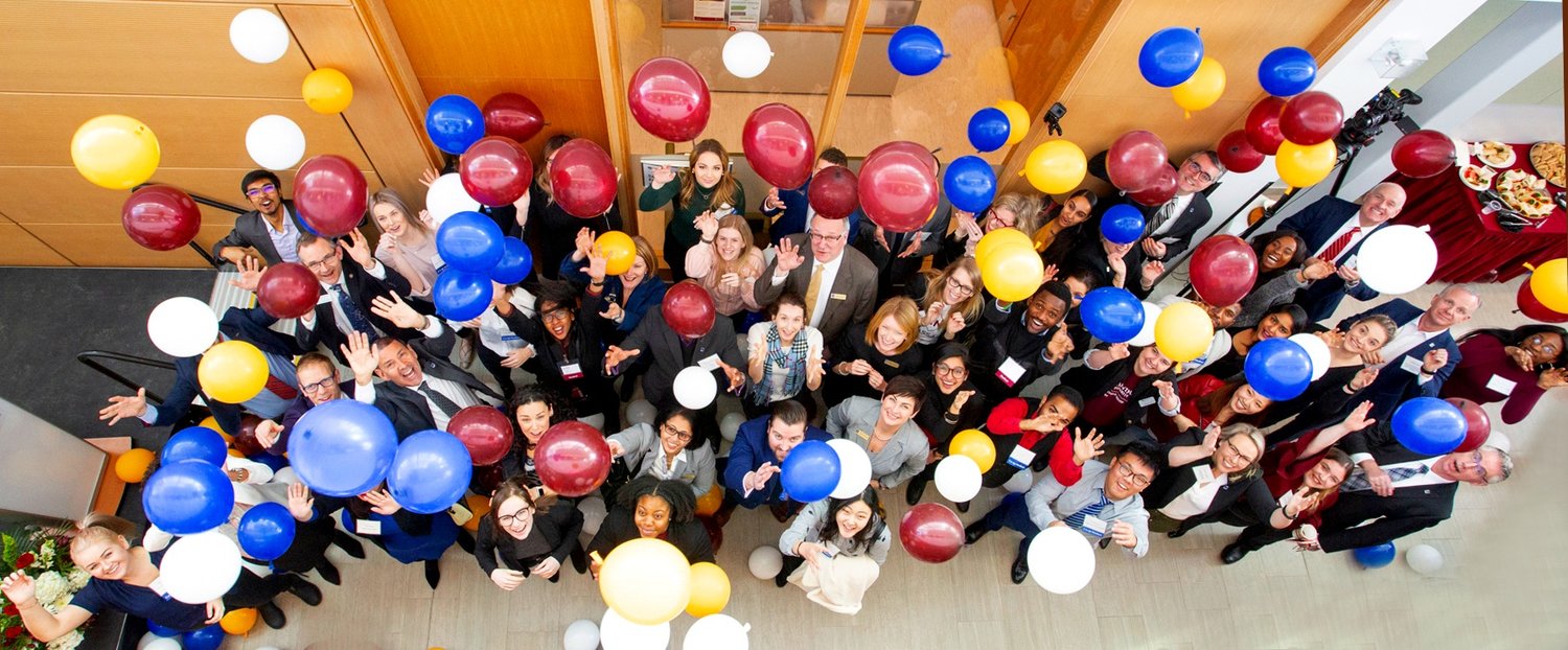 A crowd of smiling people surrounded by falling balloons.